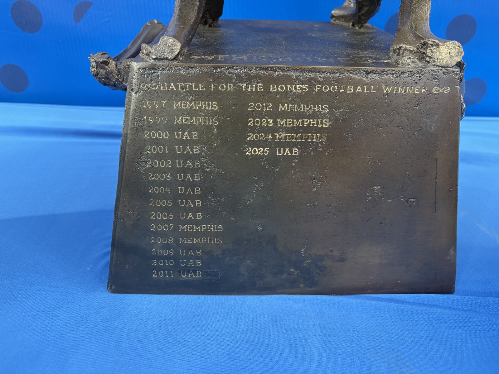 The engraved base of the Battle for the Bones trophy listing past winners from 1997 through 2025